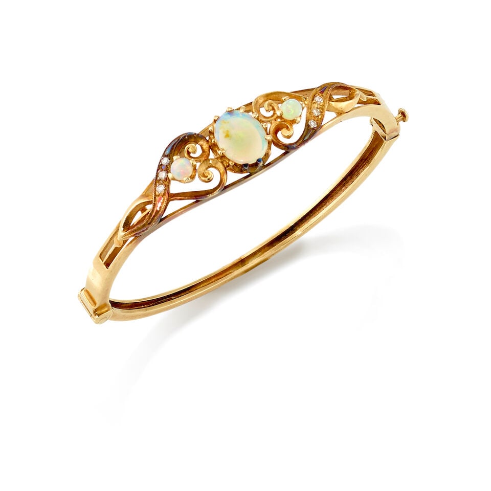 12K GOLD, OPAL, AND DIAMOND BANGLE: 12K GOLD, OPAL, AND DIAMOND BANGLE • 12K yellow gold • One oval shaped opal measuring approximately 10.37mm x 8.01mm x 195mm and two round shaped opals measuring approximately 4.26mm in