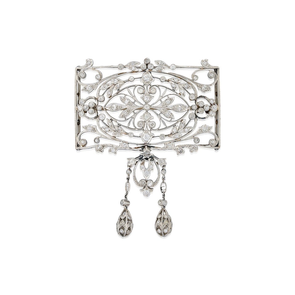 MARCUS & CO.: AN EDWARDIAN PLATINUM AND DIAMOND BROOCH: MARCUS & CO.: AN EDWARDIAN PLATINUM AND DIAMOND BROOCH The plaque brooch with floral and foliate motifs set with old European, old mine, and single-cut diamonds, suspending a central hinged drop, weig