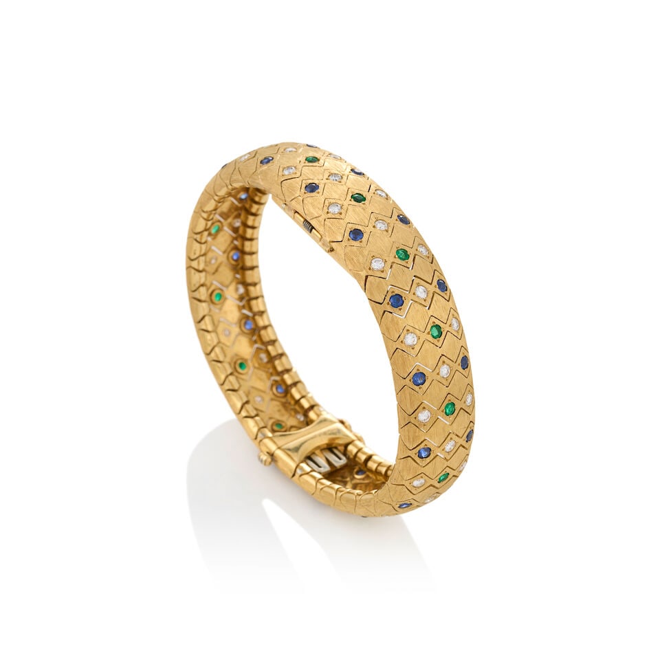 AN 18K GOLD, SAPPHIRE, EMERALD, AND DIAMOND COVERED WRISTWATCH: AN 18K GOLD, SAPPHIRE, EMERALD, AND DIAMOND COVERED WRISTWATCH The textured gold bracelet set throughout with circular-cut sapphires and emeralds and full-cut diamonds, approximate total diamond