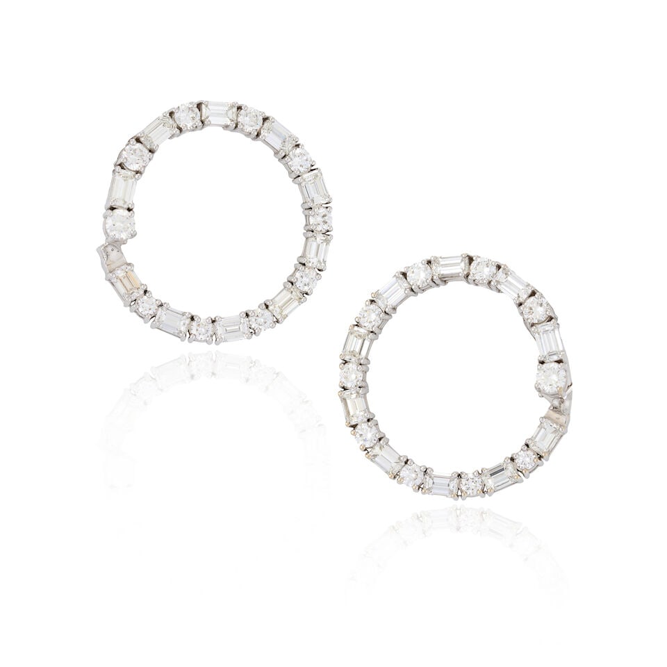 A PAIR OF 18K WHITE GOLD AND DIAMOND HOOP EARRINGS: A PAIR OF 18K WHITE GOLD AND DIAMOND HOOP EARRINGS Set with full and emerald-cut diamonds, total weight 7.65 carats, weight 9.3 dwt, length 1 1/4 in. For further information on this lot please visit