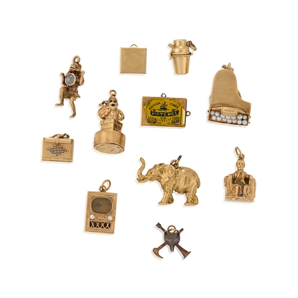 A GROUP OF MOSTLY 14K GOLD CHARMS: A GROUP OF MOSTLY 14K GOLD CHARMS Including a mechanical cocktail shaker charm, opening to reveal a red enamel devil, a dog bag charm enclosing a Terrier, two Litacharm Inc charms designed as Santa Cl