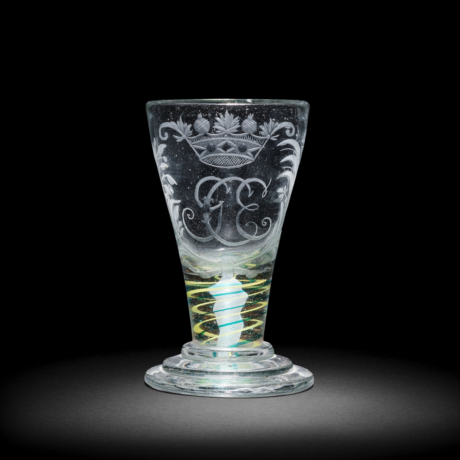 A rare Norwegian engraved yellow and green colour twist firing glass, circa 1770: A rare Norwegian engraved yellow and green colour twist firing glass, circa 1770 The conical bowl inscribed with the monogram 'GCE' beneath a crown, flanked by tied foliate branches, on a short stem c