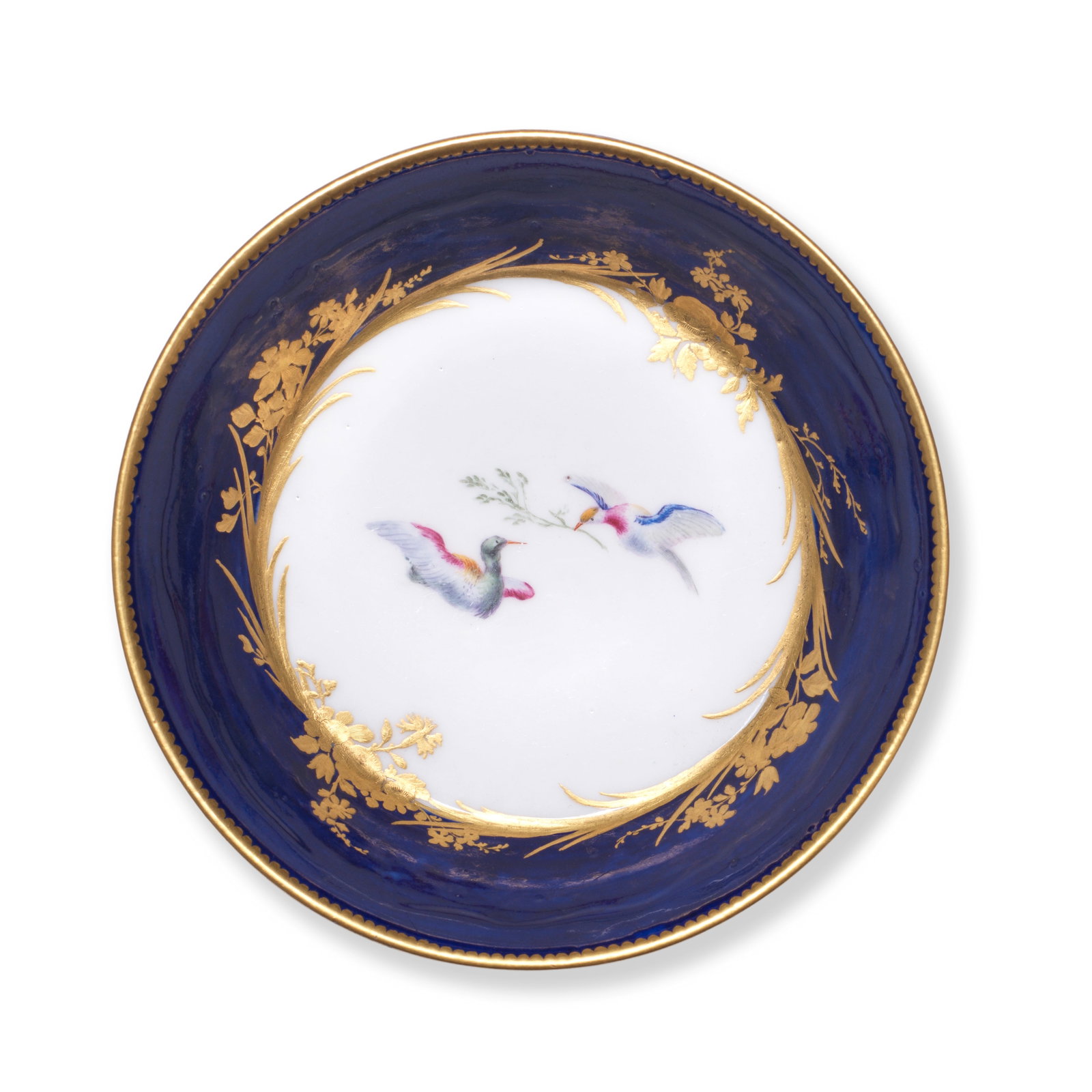 A Vincennes bleu-lapis ground saucer, circa 1750: A Vincennes bleu-lapis ground saucer, circa 1750 Painted in the centre with two coloured birds in a circular reserve edged with gilt foliage and flowers, gilt dentil border to rim, 13.3cm across, inci