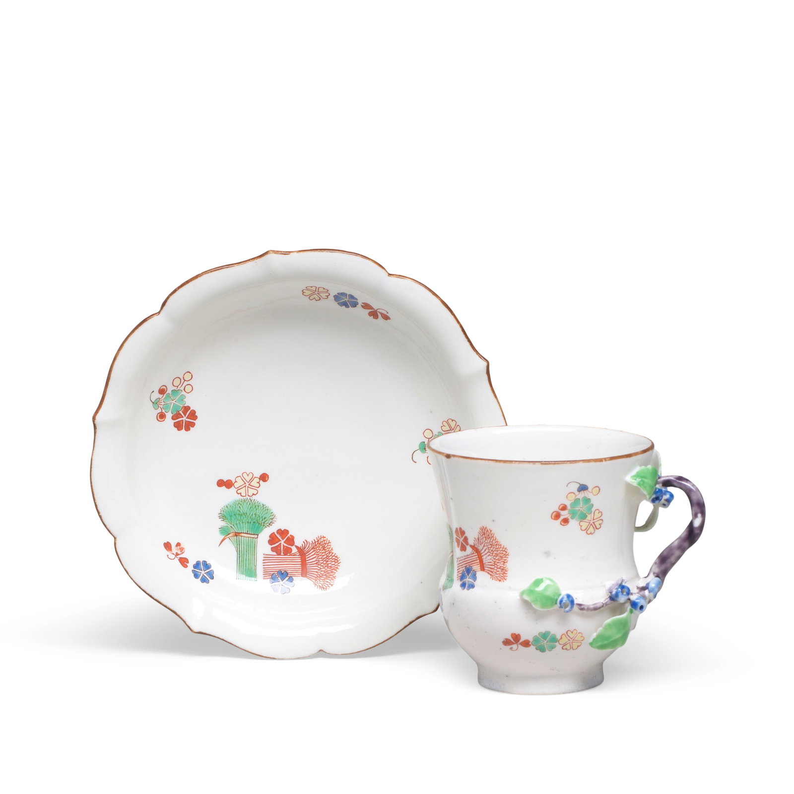 A Chantilly cup and saucer, circa 1735: A Chantilly cup and saucer, circa 1735 Painted in Kakiemon style with two banded hedges and scattered flowers, the cup with a branch handle with leafy flower-bud terminals, the saucer moulded with a f