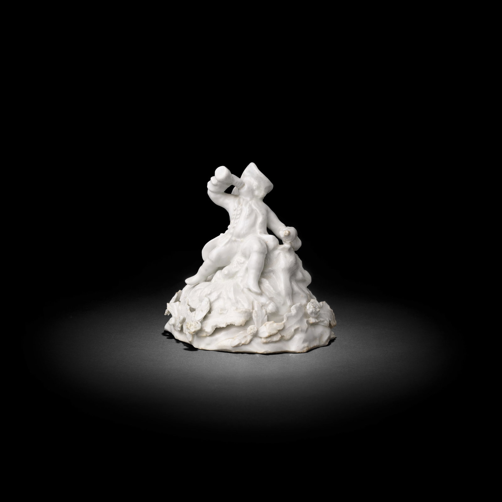 A very rare Bow white figure of a toper huntsman, circa 1752-55: A very rare Bow white figure of a toper huntsman, circa 1752-55 Modelled as a boy seated on a high mound base applied with leaves and flowers, his legs astride, a bottle raised high to his mouth in hi