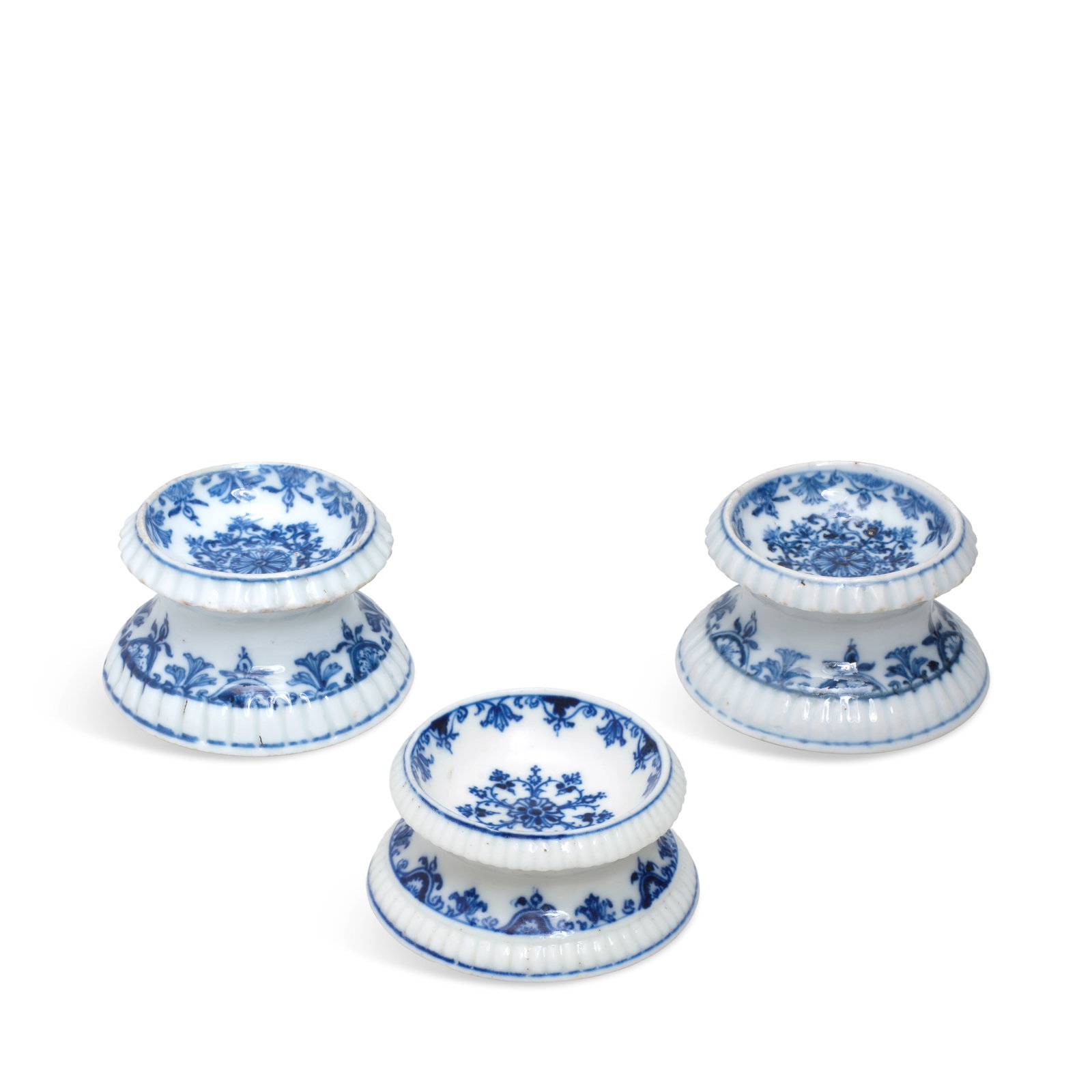A pair of Kangxi salts and a Saint-Cloud salt, circa 1715: A pair of Kangxi salts and a Saint-Cloud salt, circa 1715 The circular silver form with gadrooned band beneath rim and foot, painted in underglaze blue with lambrequin borders and a large stylised flo
