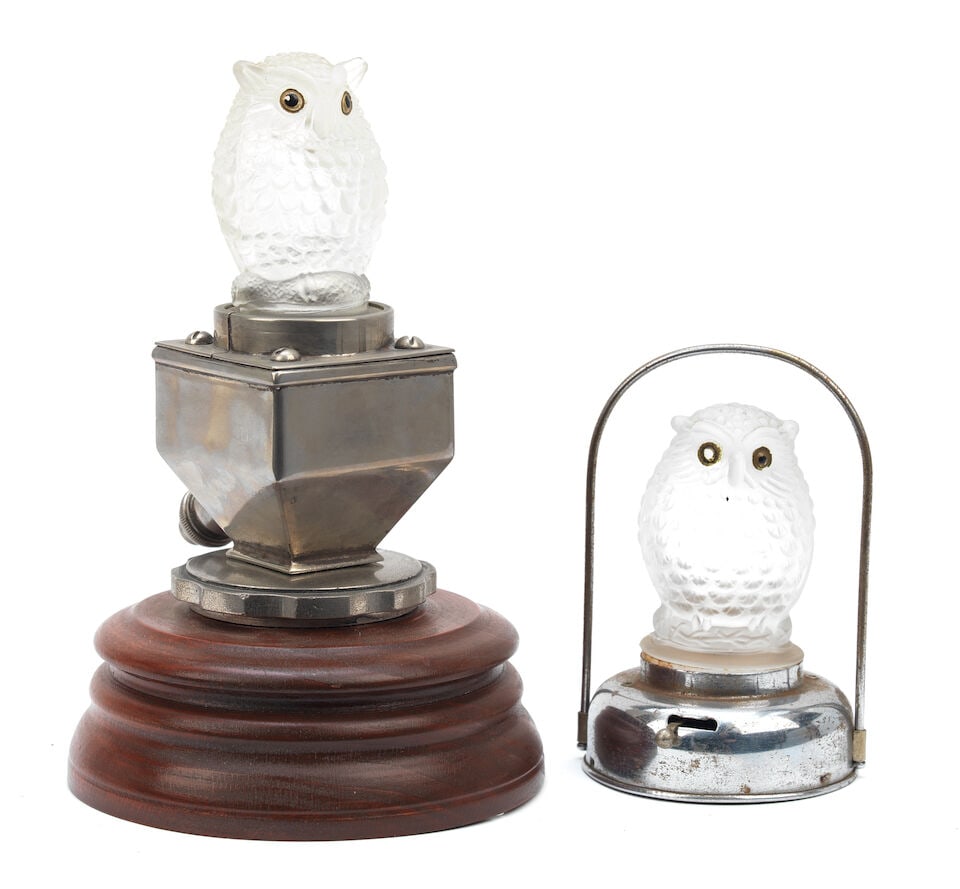 A glass owl car mascot, 1930s, ((2)): A glass owl car mascot, 1930s, moulded hollow glass 7cm high, mounted on an illuminated base, above a radiator cap on a wooden display stand, 20cm high overall, together with a similar hollow glass ow