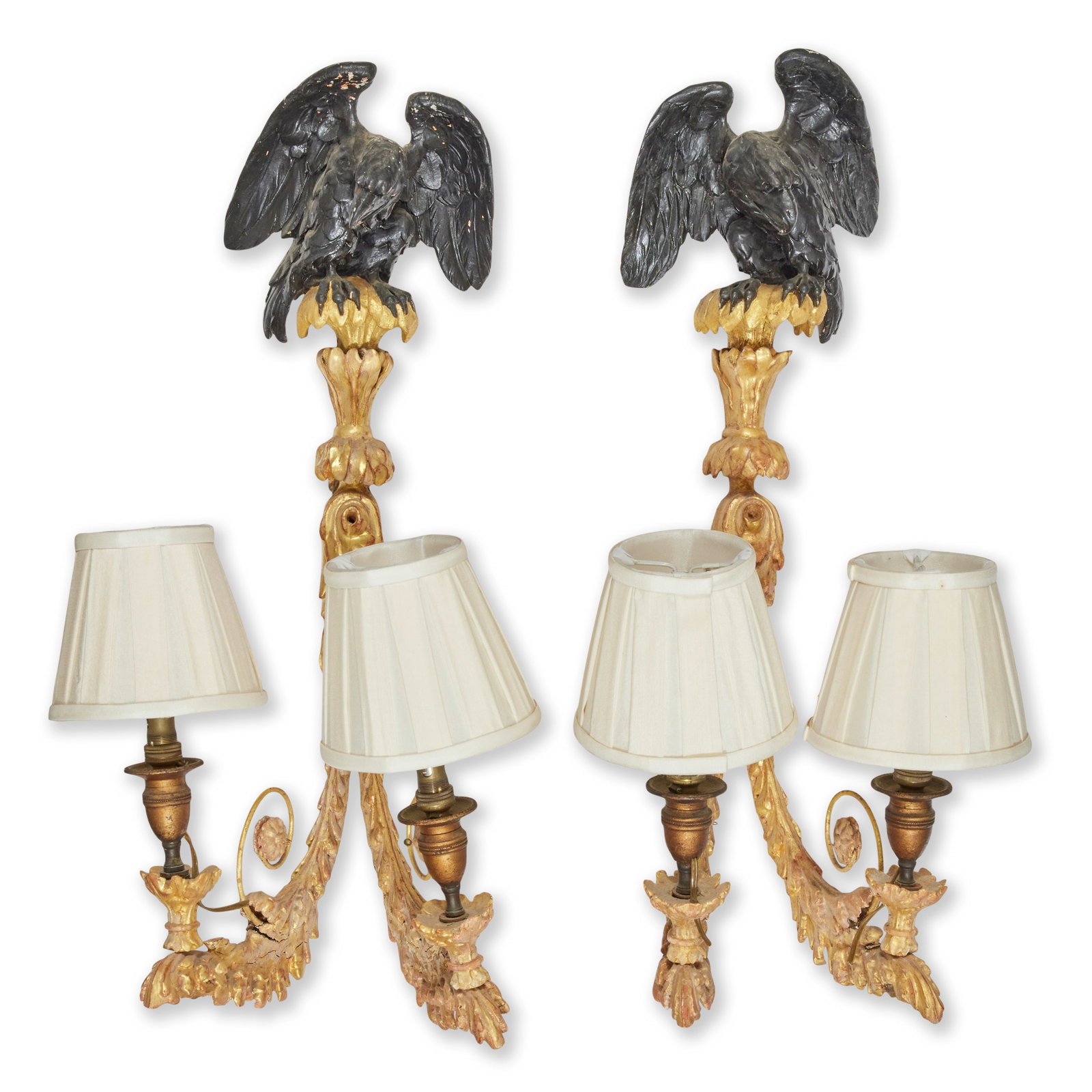 A pair of Regency carved giltwood and gesso twin branch wall lights Early 19th century (2): A pair of Regency carved giltwood and gesso twin branch wall lights Early 19th century Surmounted with ebonised eagles with later brass candle sconces and later adapted for electricity, 23cm wide, 26c