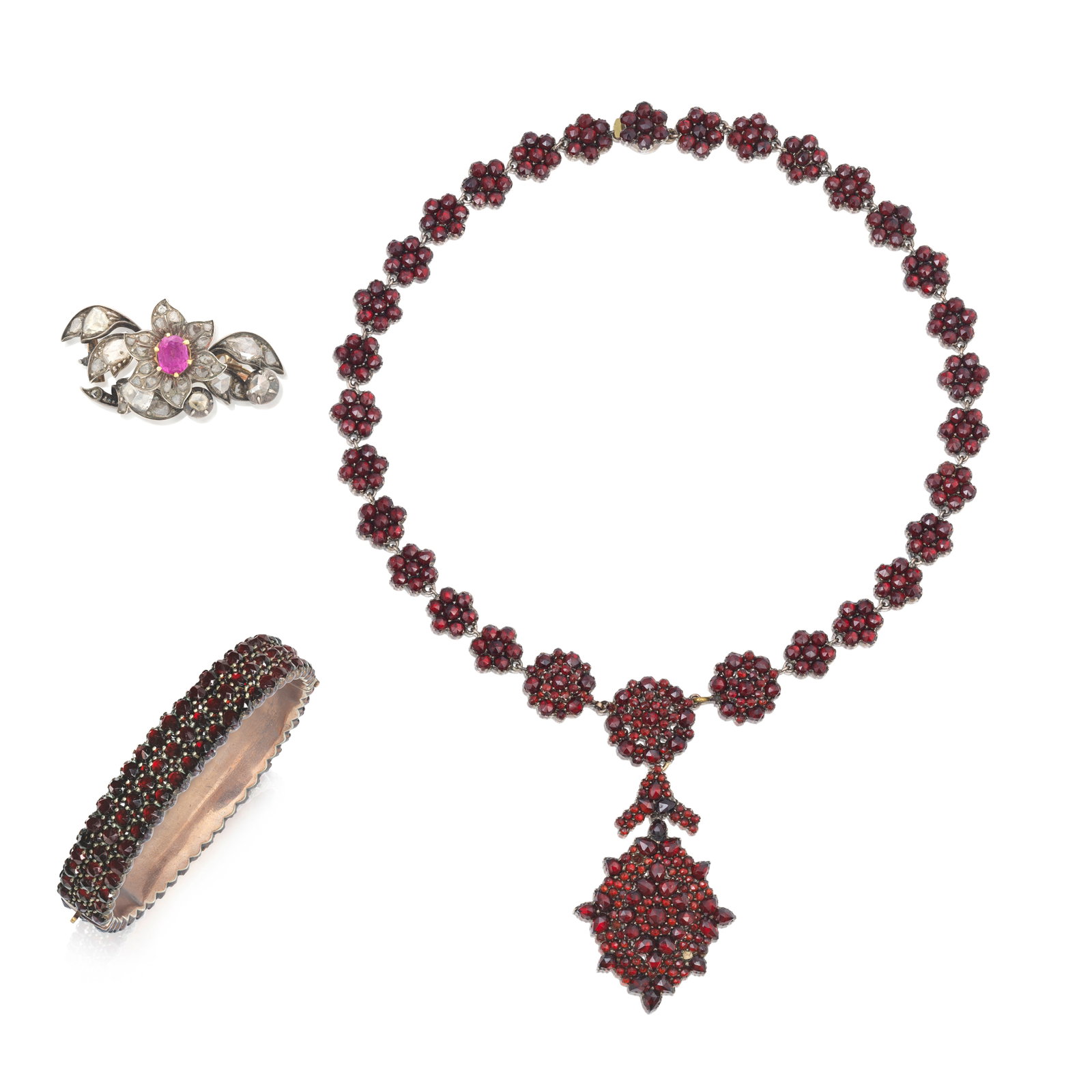 RUBY AND DIAMOND BROOCH AND GARNET NECKLACE AND BANGLE: RUBY AND DIAMOND BROOCH AND GARNET NECKLACE AND BANGLE 1st: The oval-cut ruby to a surround of rose-cut diamond petals, between leaves of similarly-cut diamonds, 2nd: The necklace designed as clusters