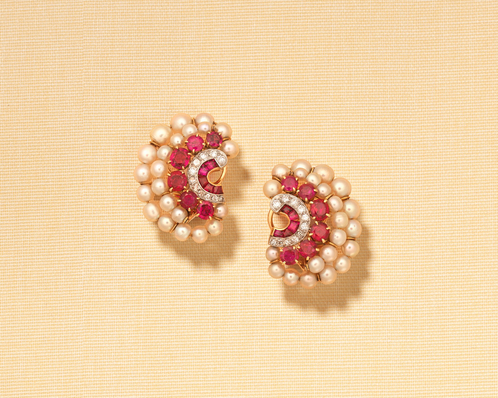CHAUMET: PEARL, RUBY AND DIAMOND EARCLIPS, MID 2OTH CENTURY: CHAUMET: PEARL, RUBY AND DIAMOND EARCLIPS, MID 2OTH CENTURY Of scroll design, composed of rows of pearls, circular and calibré rubies and brilliant and single-cut diamonds, maker's mark JC, Frenc