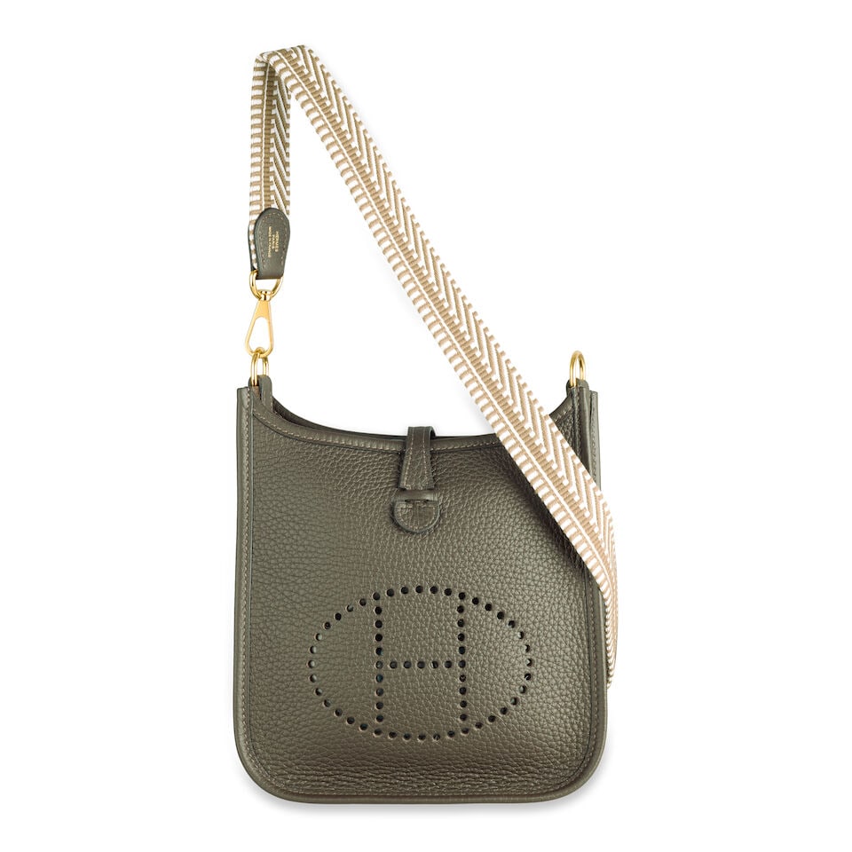 Hermès: an Ebene Clemence Leather Evelyne TPM 16 2024 (includes dust bags, care card and box): Hermès: an Ebene Clemence Leather Evelyne TPM 16 2024 Gold tone hardware, with Gris Pale and Etoupe canvas shoulder strap Condition Grade A- 16cm wide, 18cm high, 55cm shoulder drop, includes dus