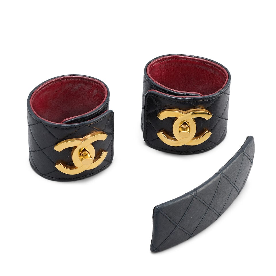 Chanel: a Pair of Black Quilted Leather Cuffs and a Matching Barrette 1990s: Chanel: a Pair of Black Quilted Leather Cuffs and a Matching Barrette 1990s Creative Director: Karl Lagerfeld Quilted lambskin cuffs with red leather lining, gold tone CC twist locks at each wrist, 5.