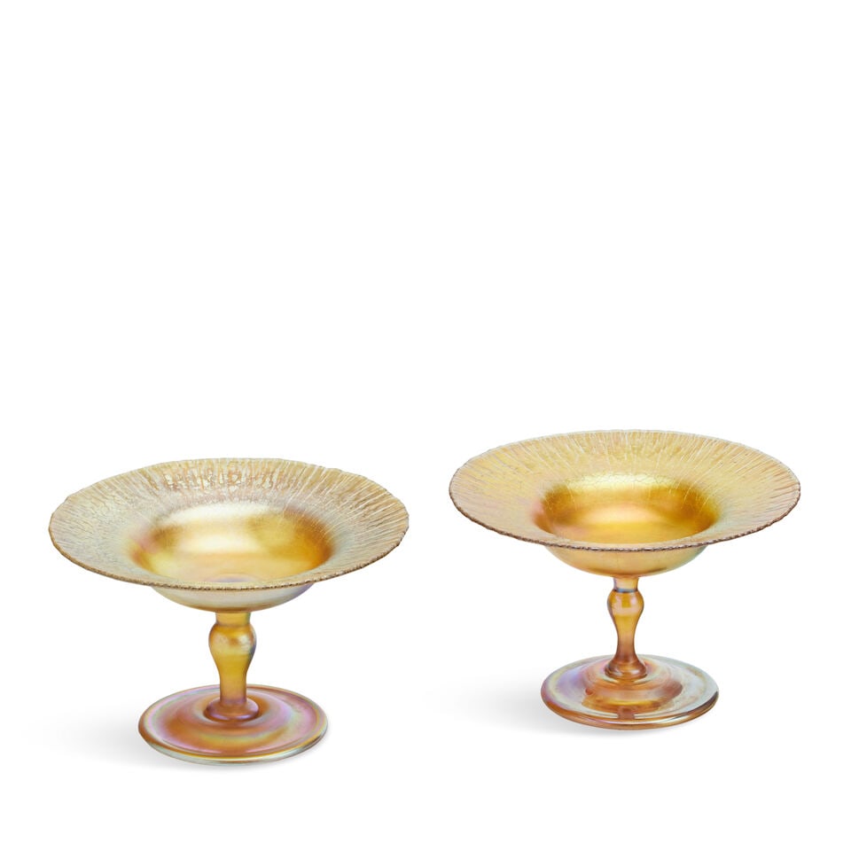 Two Tiffany Studios favrile glass compotes 1899-1918: Two Tiffany Studios favrile glass compotes 1899-1918 Each with narrow baluster stem and shallow bowl and gold lustre finish (2) height 9.5cm, diameter 15cm engraved with L.C.T. Favrile mark For furthe