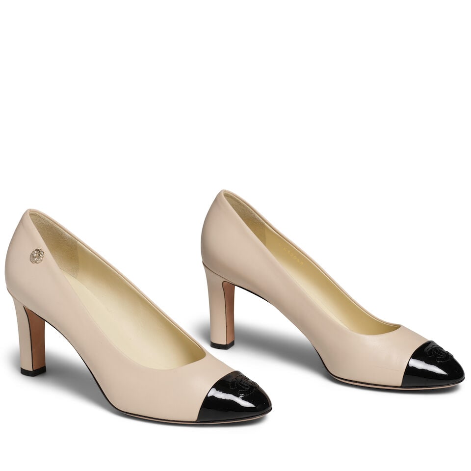 CHANEL: BEIGE AND BLACK LEATHER PUMPS: CHANEL: BEIGE AND BLACK LEATHER PUMPS • Beige Leather Exterior and Black Patent Leather Toe • Interlocking CC Logo at Toe • Silver Camellia Charm Detail • Marked Size 40.5 For 