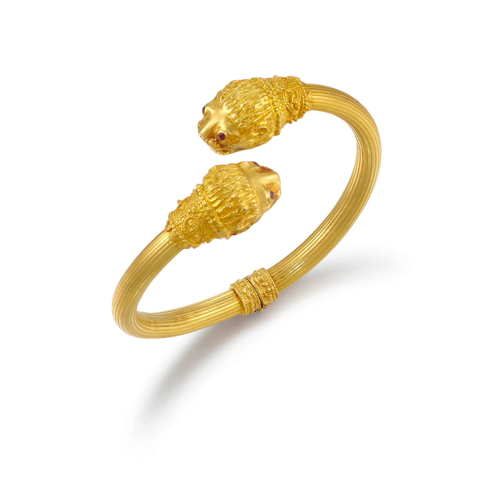 AN 18K GOLD AND RUBY BRACELET: AN 18K GOLD AND RUBY BRACELET A hinged bangle with lions' head terminals, accented with round ruby eyes; with partial maker's mark; inner circumference 6 1/2 in. Footnotes: OVERALL CONDITION: Metal st