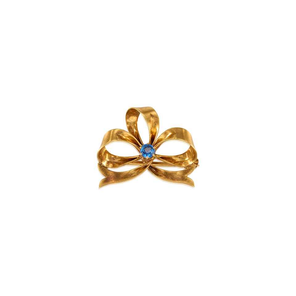 TIFFANY & CO.: 18K YELLOW GOLD AND SAPPHIRE BOW BROOCH: TIFFANY & CO.: 18K YELLOW GOLD AND SAPPHIRE BOW BROOCH • A round shaped sapphire measuring approximately 3.63mm in diameter • Stamped TIFFANY & CO. • Measures 1 in. x 3/4 in. •