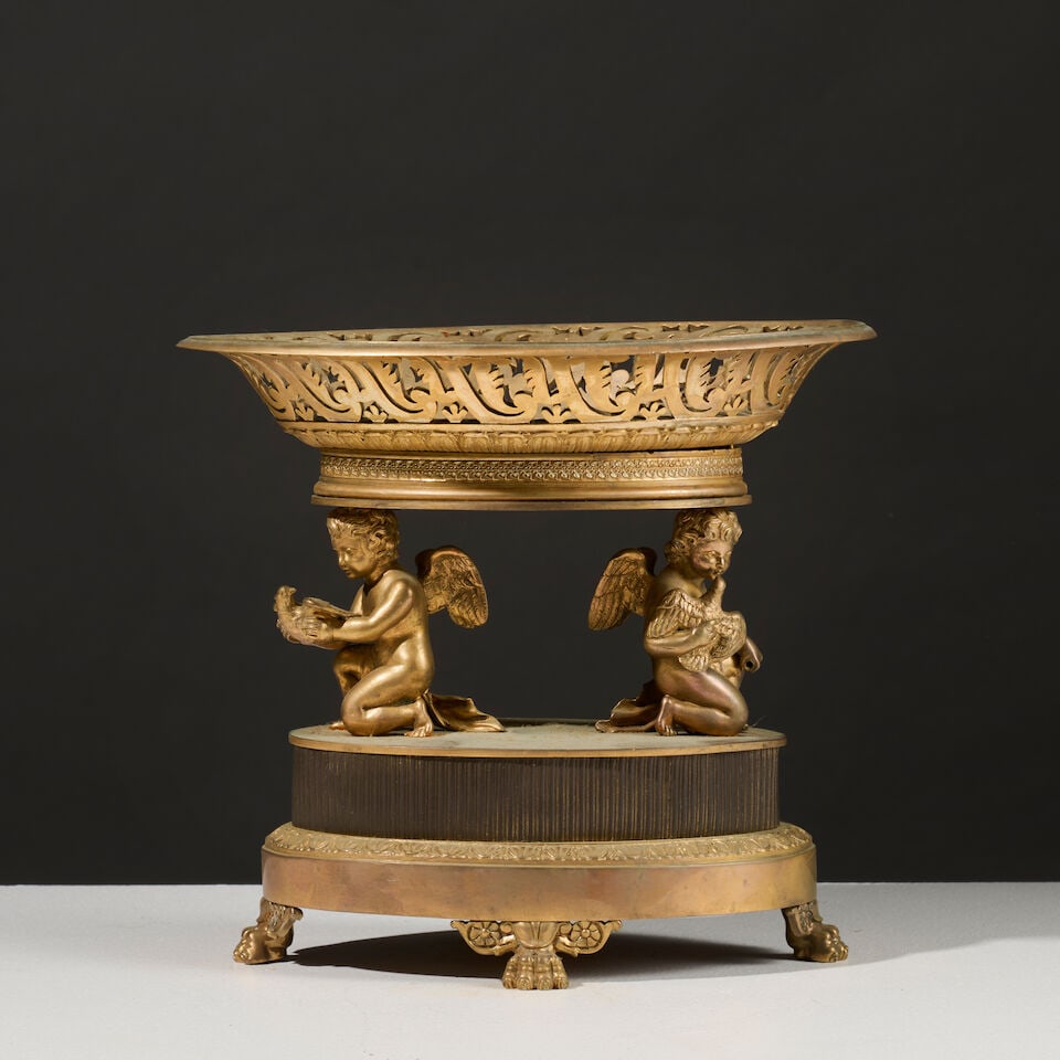 Vide poche de forme navette en bronze doré et patiné, les montants en forme d'amours j...: Vide poche de forme navette en bronze doré et patiné, les montants en forme d'amours jouant d'époque Restauration A shuttle-shaped trinket tray in gilt and patinated bronze, the sides
