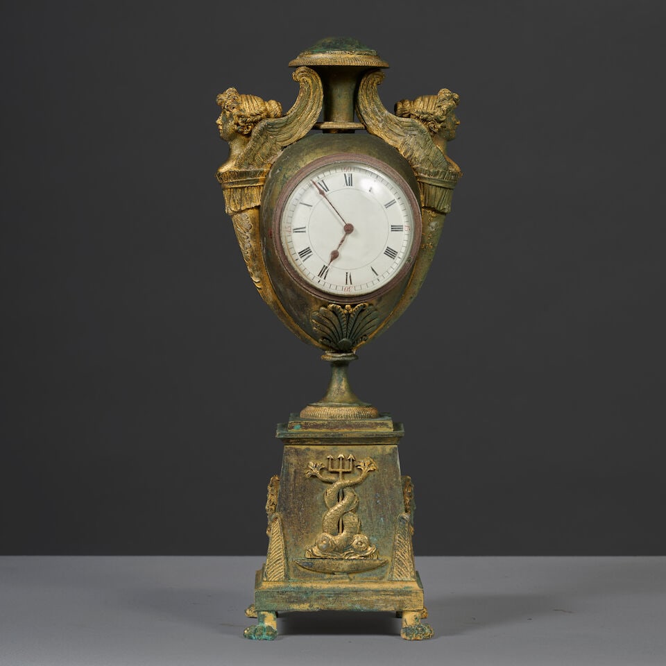 Pendule en forme de vase en bronze doré et patiné d'époque Empire An Empire vase-...: Pendule en forme de vase en bronze doré et patiné d'époque Empire An Empire vase-shaped clock in gilt and patinated bronze Le cadran et le mouvement sont inscrit dans le corps de vase,
