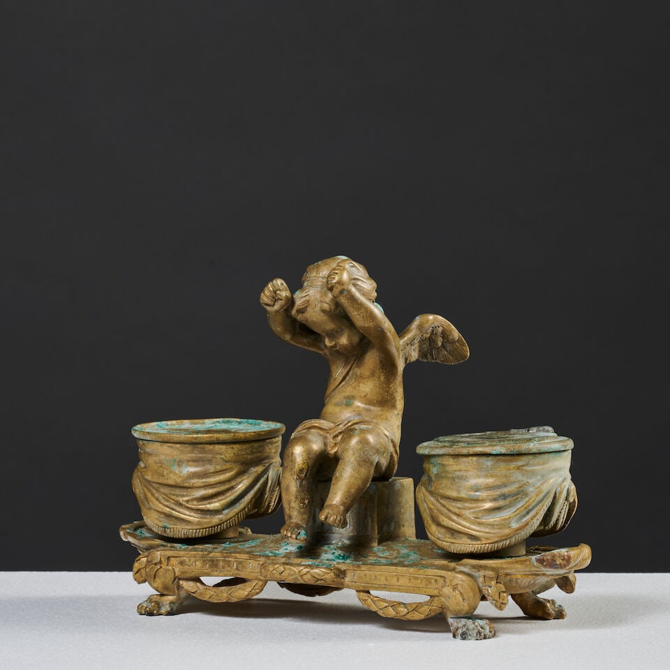 Encrier en bronze doré et ciselé figurant un angelot aux tambours, XIXe siècle A ...: Encrier en bronze doré et ciselé figurant un angelot aux tambours, XIXe siècle A chased gilt-bronze inkwell depicting a cherub with drums, 19th century L'angelot assis est encadré 