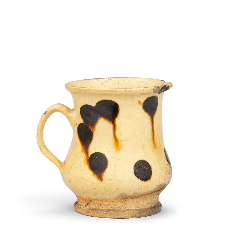A Staffordshire slipware mug, late 17th or early 18th century: A Staffordshire slipware mug, late 17th or early 18th century Of gentle bell shape with an everted rim and generous loop handle, the buff body covered with a cream-coloured slip and decorated with two