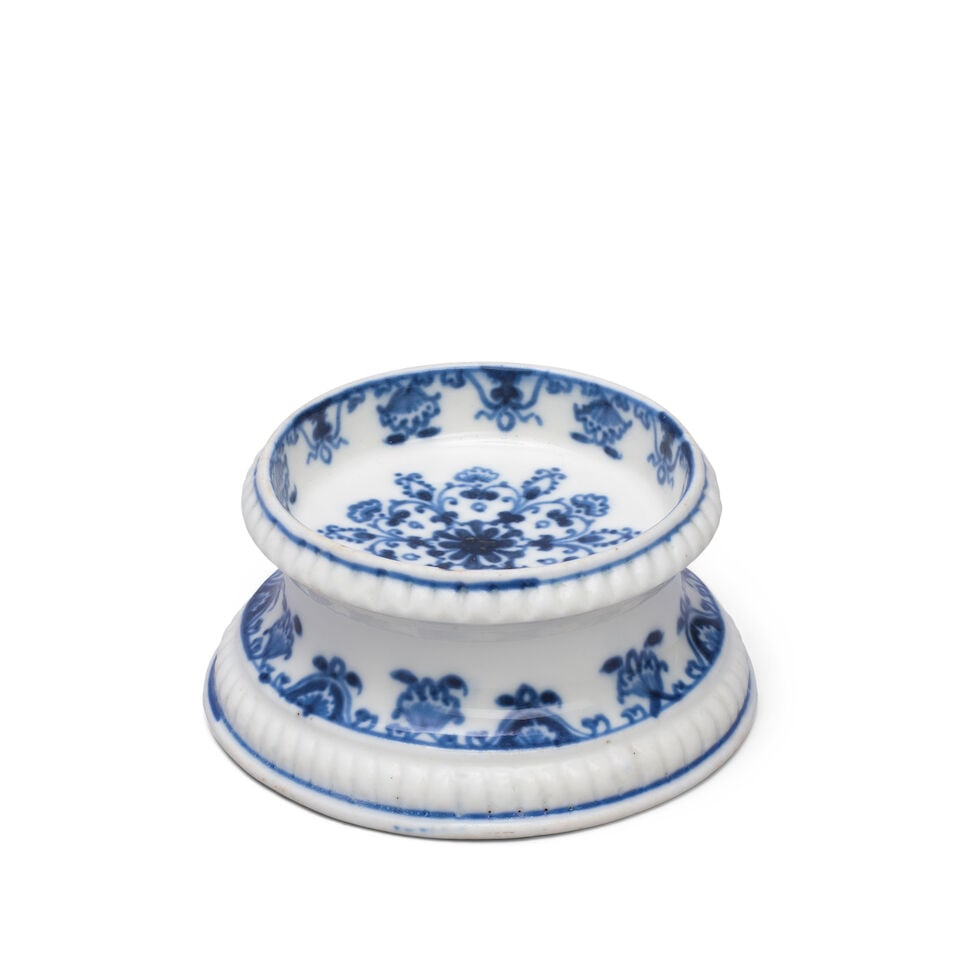 A Saint-Cloud salt, circa 1710-20: A Saint-Cloud salt, circa 1710-20 The circular silver form with gadrooned band beneath rim and foot, painted in underglaze blue with lambrequin borders and a large stylised floral motif in the