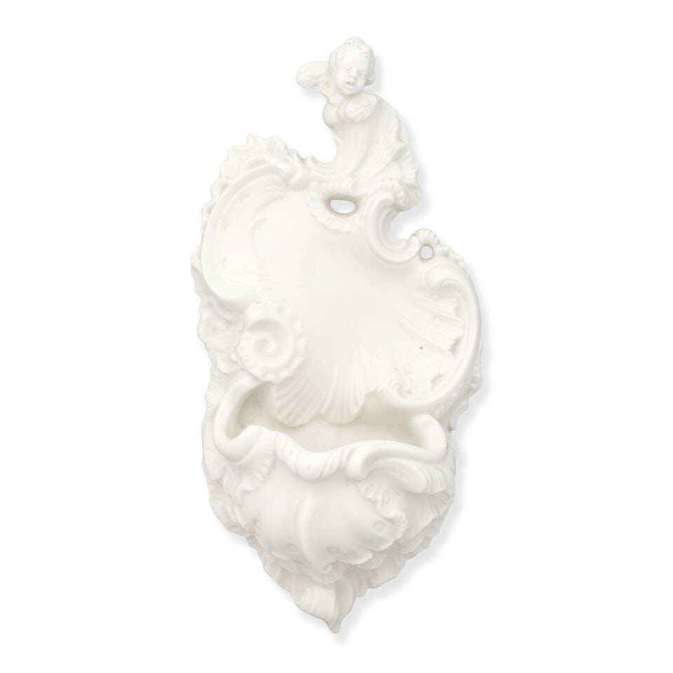 A Nymphenburg holy water stoop, 20th century: A Nymphenburg holy water stoop, 20th century After the 18th century model by F. A. Bustelli, in rococo style, moulded with scroll- and shellwork and surmounted by the winged bust of a putto, 22.5cm