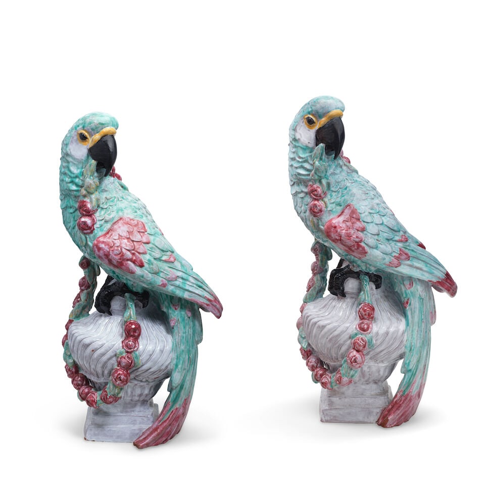 Two monumental Nymphenburg majolica macaws modelled by Josef Wackerle, 20th century: Two monumental Nymphenburg majolica macaws modelled by Josef Wackerle, 20th century Each holding a flower garlands in its beak and perched on an urn, the plumage decorated in shades of turquoise and