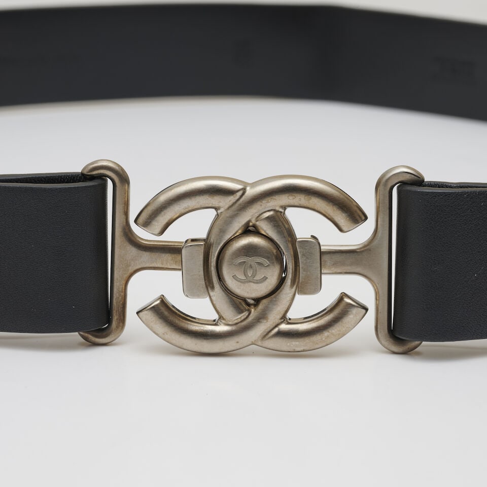 Chanel, année 2015. Ceinture en cuir noir à boucle façon fermoir de sac. Chanel, ...: Chanel, année 2015. Ceinture en cuir noir à boucle façon fermoir de sac. Chanel, 2015. Black leather belt with a buckle styled like a bag clasp. Directeur artistique: Karl Lagerfeld. Ta