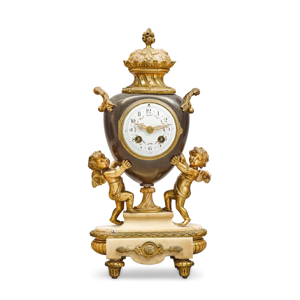 A late 19th century gilt and patinated bronze figural mantel clock In the Louis XV style: A late 19th century gilt and patinated bronze figural mantel clock In the Louis XV style The pedestal urn case with foliate handles surmounted by a figural canopy, the white enamel dial with Arabic
