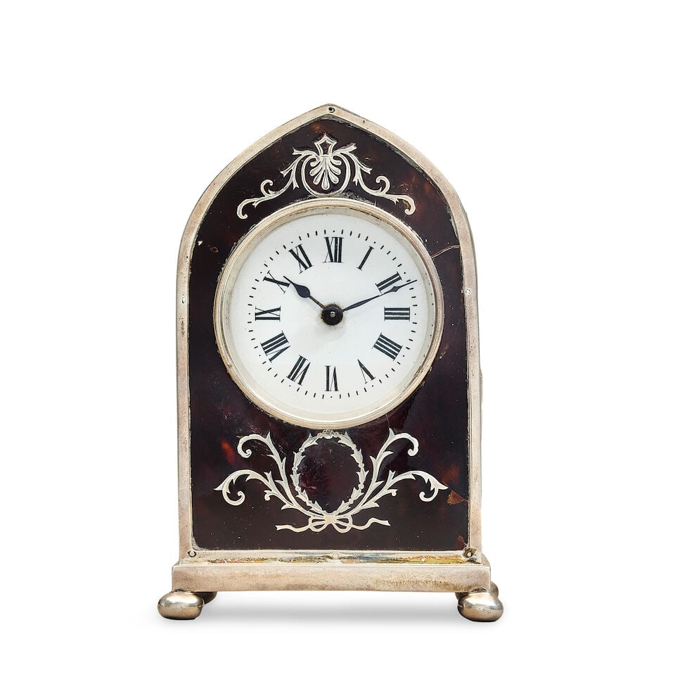 An Edwardian William Comyns silver mounted and inlaid tortoiseshell mantel timepiece: An Edwardian William Comyns silver mounted and inlaid tortoiseshell mantel timepiece The lancet arched case on ball feet, the front panel with stylised anthemion and scrolling inlaid cresting above a 