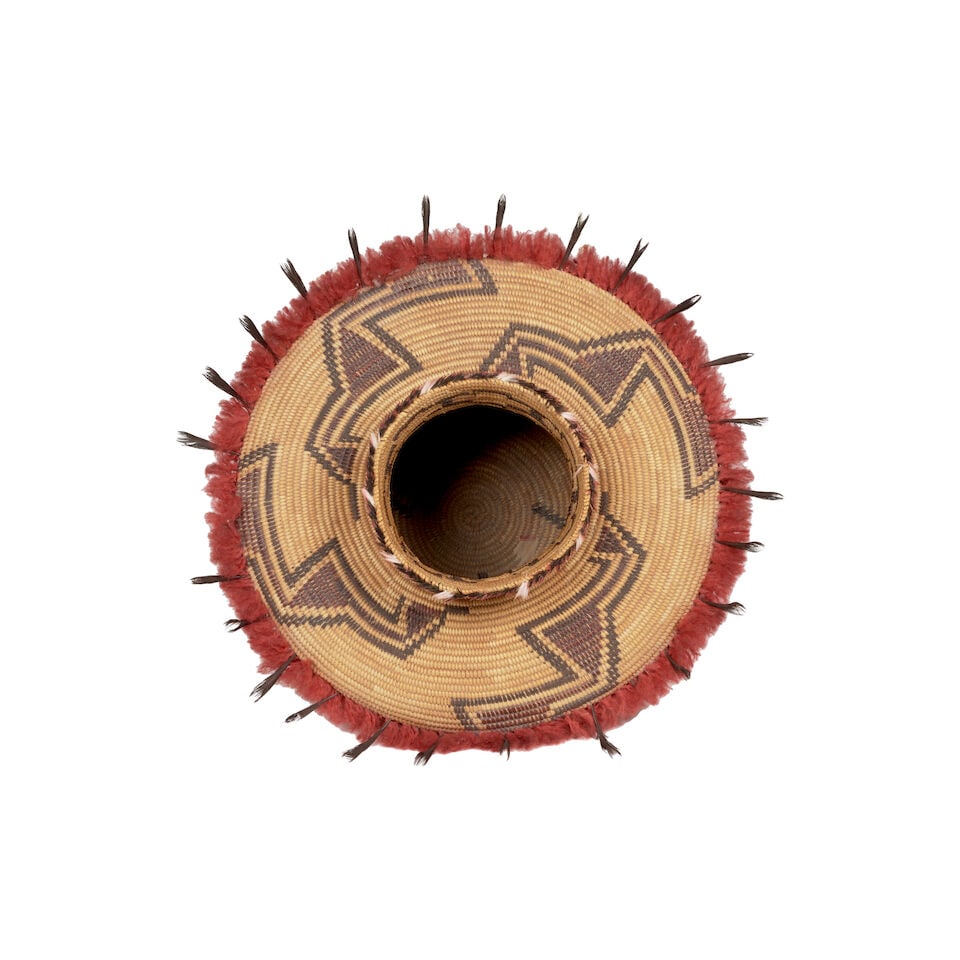 A Yokuts polychrome bottleneck basket: A Yokuts polychrome bottleneck basket A quartet of diagonal stepped meanders originating from the base, a fretwork band about the neck, yarn fringe and quail topknots encircling the shoulder, noted