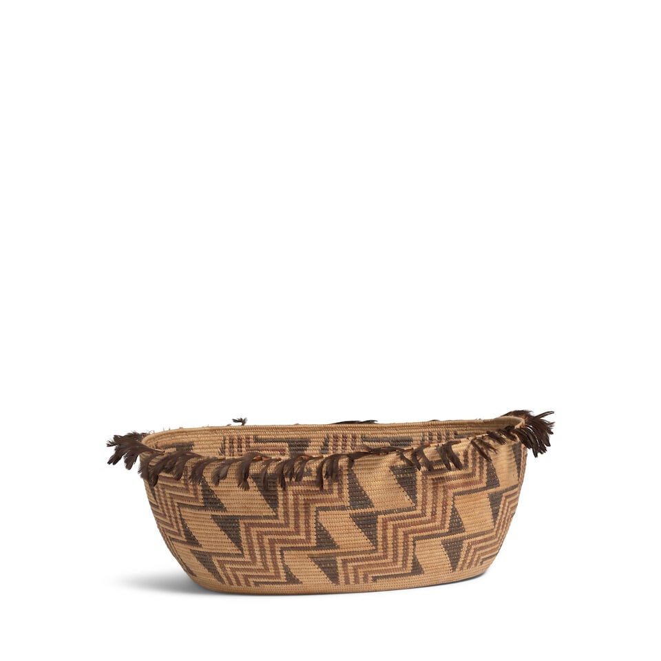 A Yokuts polychrome oval basket: A Yokuts polychrome oval basket Woven in a dense pattern of stairstep diagonal bands alternating with zigzag fields, cruciform motifs encircling the center, quail topknots about the perimeter of the