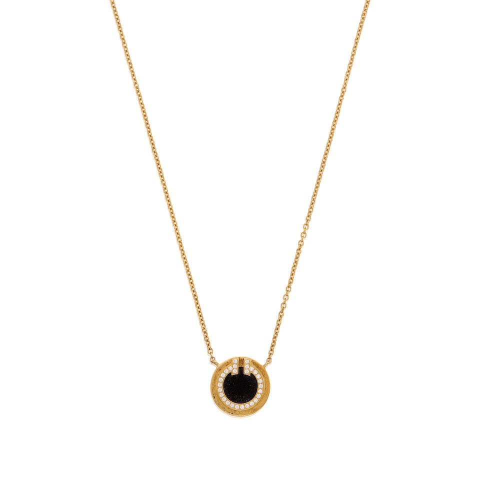 TIFFANY & CO.: A 18K YELLOW GOLD 'TIFFANY T' ONYX AND DIAMOND PENDANT NECKLACE: TIFFANY & CO.: A 18K YELLOW GOLD 'TIFFANY T' ONYX AND DIAMOND PENDANT NECKLACE • Numerous round shaped diamonds weighing approximately 0.05 carat total • One round shaped onyx measuring ap