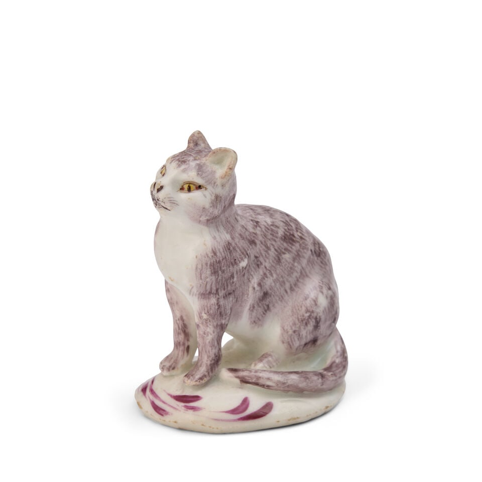 A Bow Porcelain Model of a Seated Cat circa 1758-60: A Bow Porcelain Model of a Seated Cat circa 1758-60 Its fur delicately painted in pale puce, its eyes in red and yellow, on an oval base with puce scrolls. height 2 5/8 in. (6.67 cm.); width 1 1/2 in.
