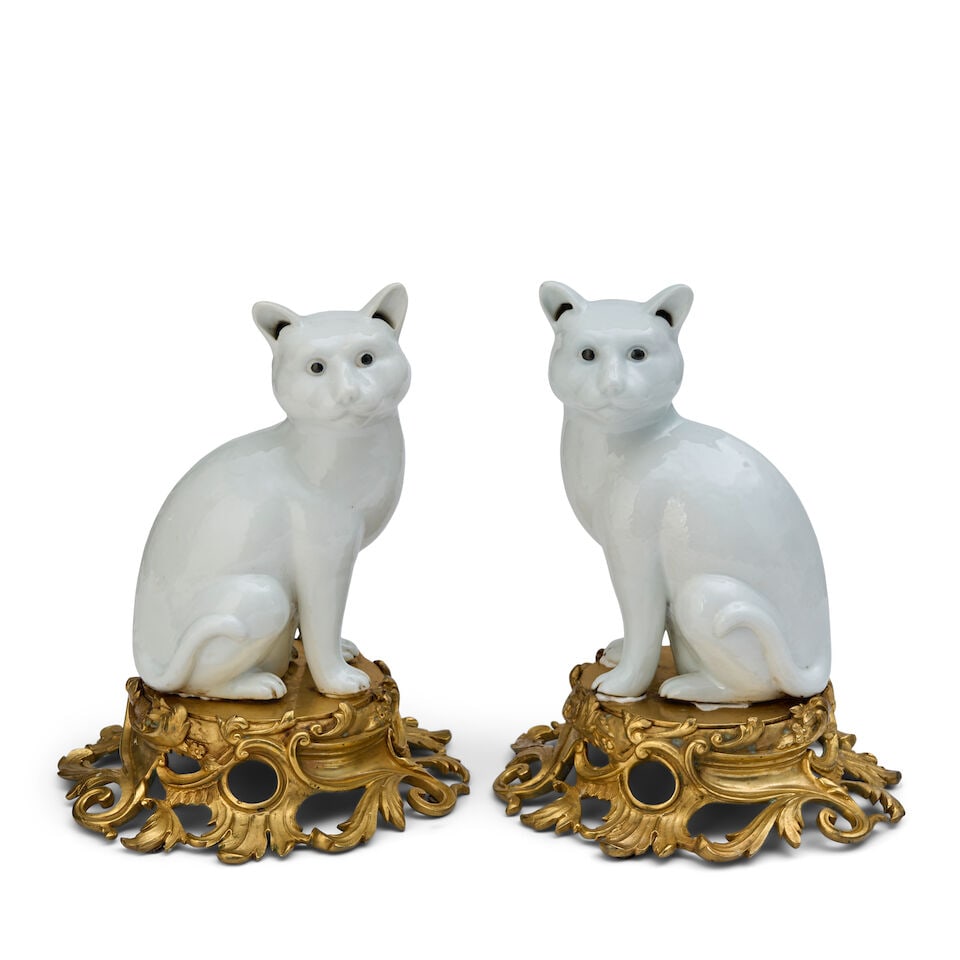 A Pair of Porcelain Models of Seated Cats Japan, circa 1900: A Pair of Porcelain Models of Seated Cats Japan, circa 1900 Mirroring each other in seated pose and decorated with an allover white glaze, mounted on ormolu bases. each height 10 1/4 in. (26.04 cm.); 