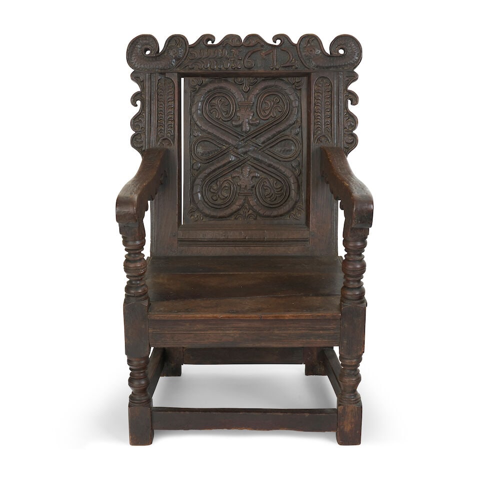 An English 17th century oak wainscot armchair: An English 17th century oak wainscot armchair the carved cresting with stylised sea serpents flanking the raised date '1672', above interlaced strapwork back panel, the shaped arms supported on