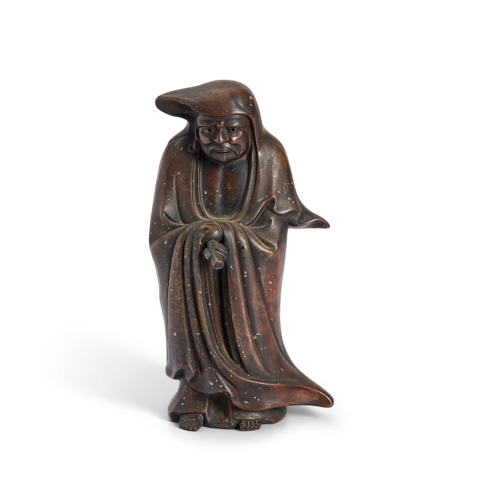 A Bronze Figure of Daruma Japan, late Edo period (1615-1868) or Meiji era (1868-1912), 19th/20th...: A Bronze Figure of Daruma Japan, late Edo period (1615-1868) or Meiji era (1868-1912), 19th/20th century, Depicted standing holding a scroll in one hand, wearing flowing robes 10in (25.4cm) high For