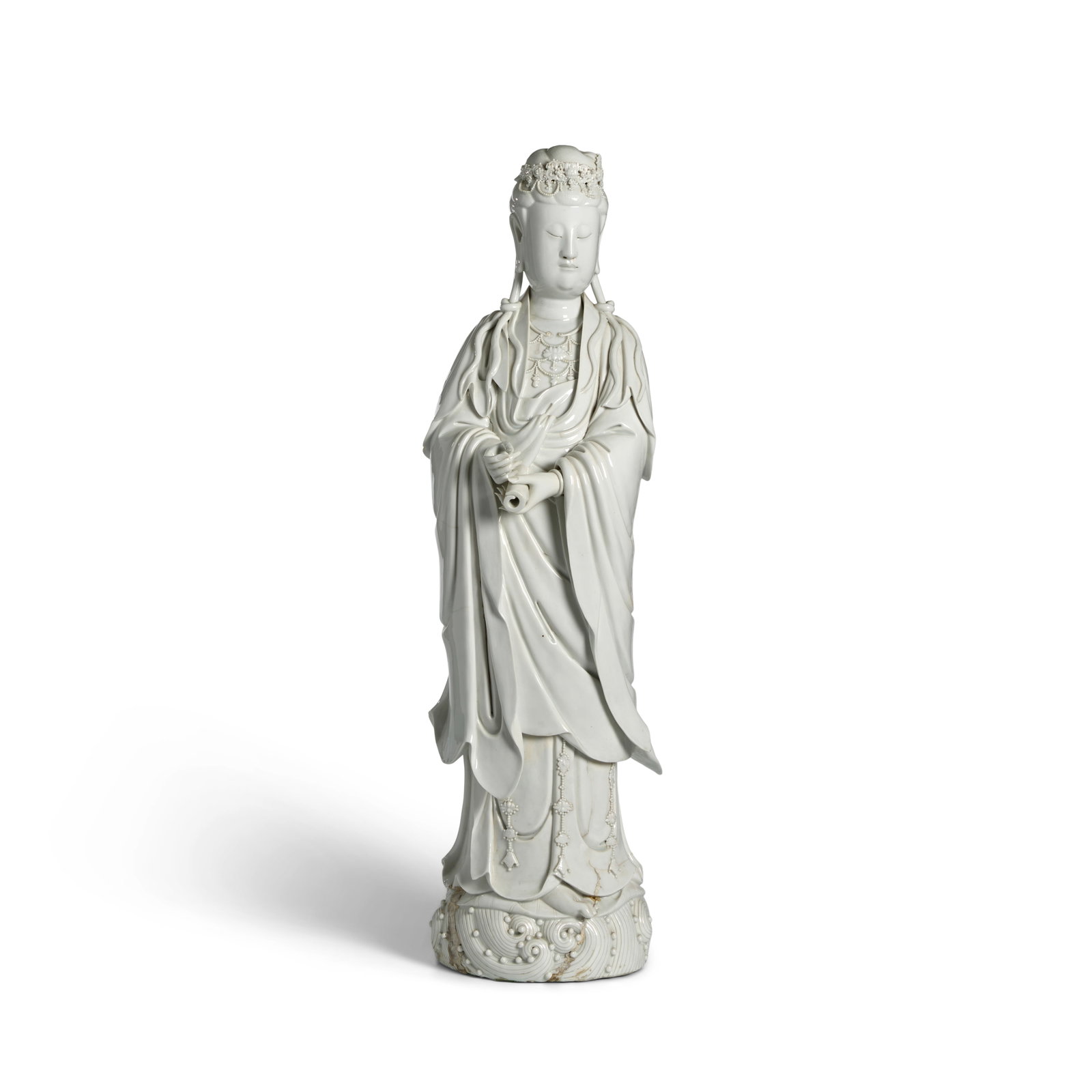 AN IMPRESSIVE LARGE DEHUA WHITE-GLAZED FIGURE OF GUANYIN 18th century: AN IMPRESSIVE LARGE DEHUA WHITE-GLAZED FIGURE OF GUANYIN 18th century The serene figure standing on a base of swirling clouds, the hands holding a scroll in front of the body, hidden under voluminous 