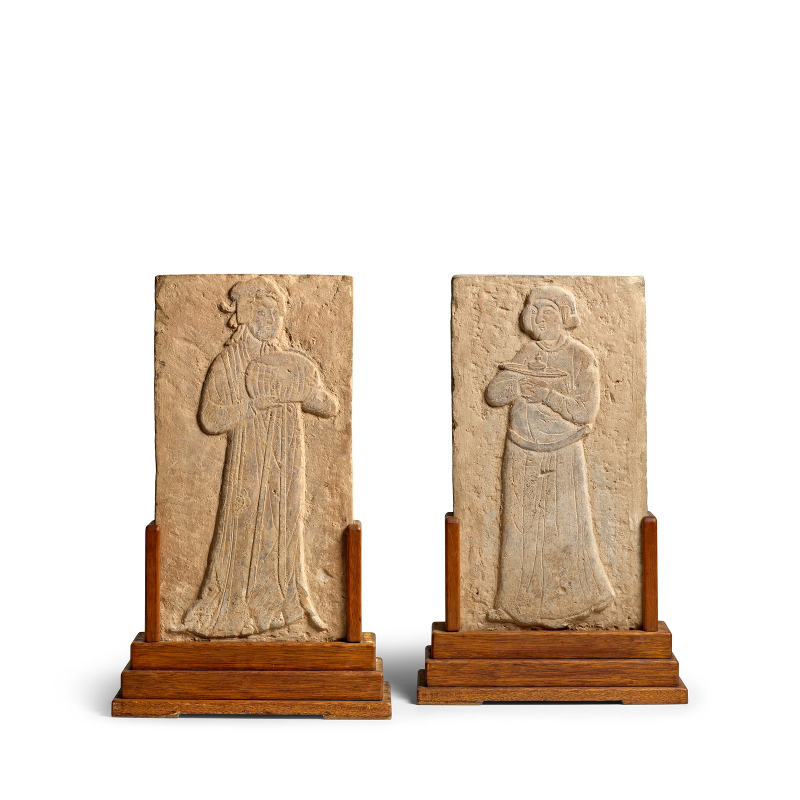 A PAIR OF MOLDED 'ATTENDANT' POTTERY PANELS Song Dynasty (2, wood stands): A PAIR OF MOLDED 'ATTENDANT' POTTERY PANELS Song Dynasty One depicting a young servant holding a small vase atop a footed tray, his hair neatly bundled behind the ears, facing slightly to the left sho