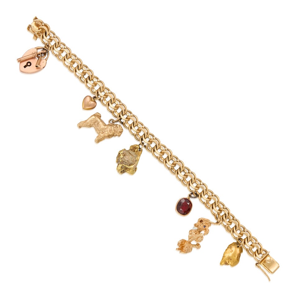 A GOLD CHARM BRACELET: A GOLD CHARM BRACELET • 13K gold bracelet with one 9K, one 13K, one 14K, one 18K, one 21K gold, three 14K rose gold and one iron-based metal charms • One cushion-shaped garnet weighing