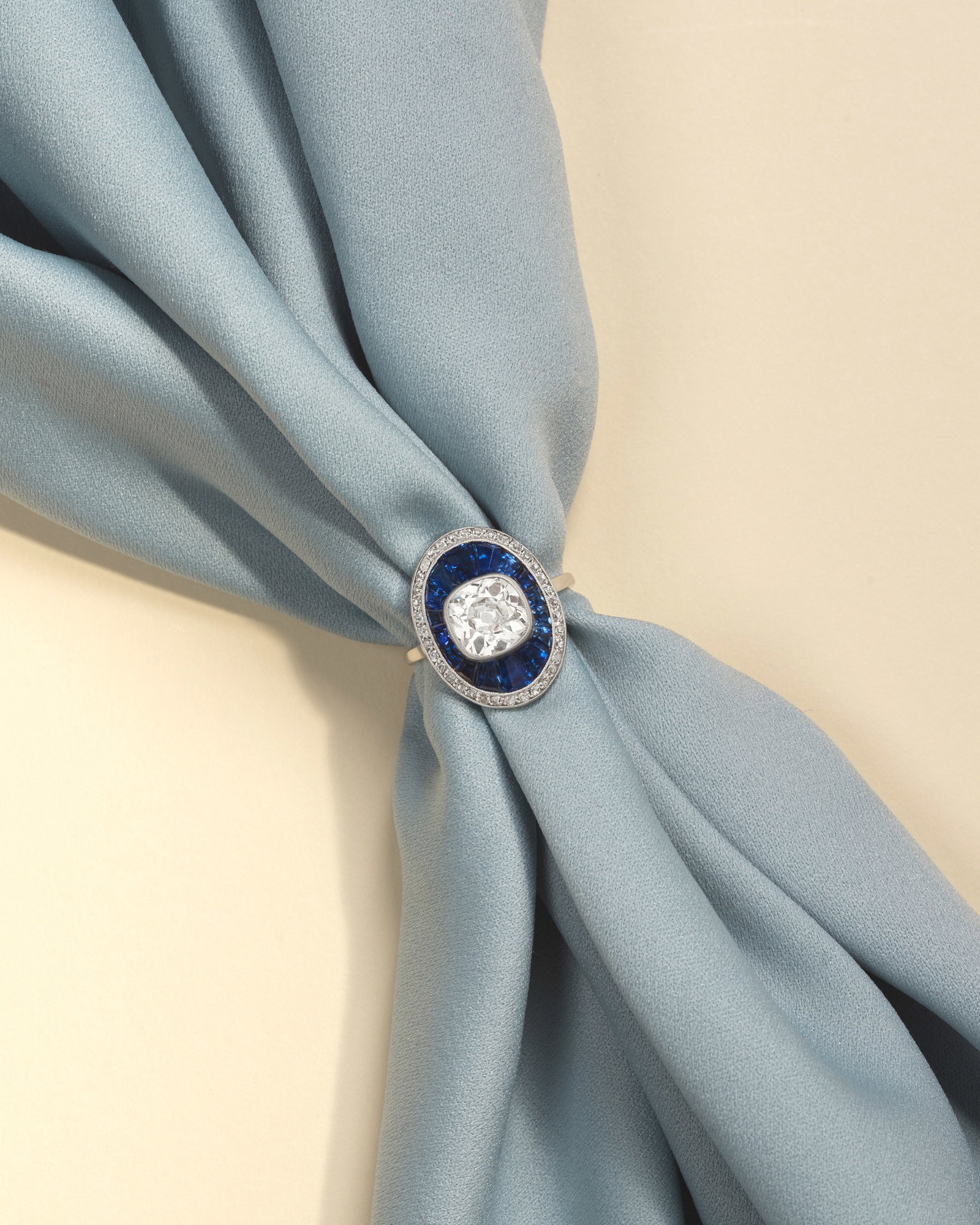 DIAMOND AND SAPPHIRE RING, CIRCA 1910: DIAMOND AND SAPPHIRE RING, CIRCA 1910 The old cushion-cut diamond millegrain-set within a border of radiating calibré-cut sapphires, to a surround of old single-cut diamonds, principal diamond ve