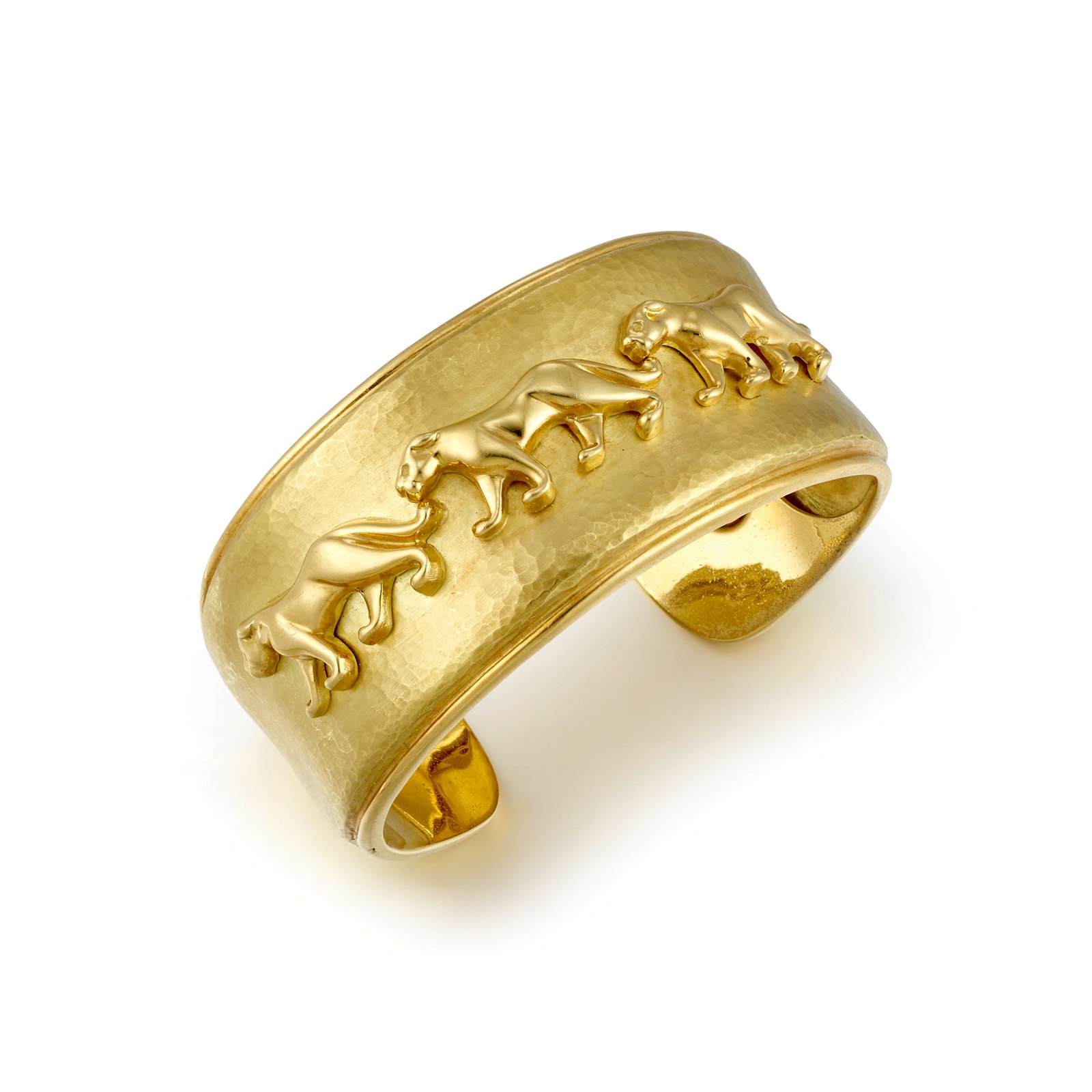 AN 18K GOLD BRACELET, ITALY: AN 18K GOLD BRACELET, ITALY A cuff bracelet of hammered finish, centering a trio of lionesses; with maker's mark; with Italian registered trademark; inner circumference 6 1/4 in., gap 7/8 in., width 1