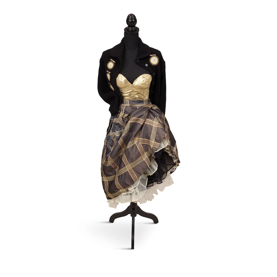 A CLOCK CARDIGAN LOOK 1980s, styled by Cyndi Lauper: A CLOCK CARDIGAN LOOK 1980s, styled by Cyndi Lauper Comprising a black knit cardigan decorated with rhinestone clocks, a gold bustier, a grey trimmed taffeta skirt, a black petticoat, and an off-white