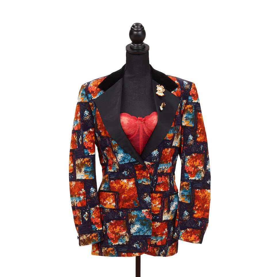 A MAGAZINE-WORN PIN-DECORATED BLAZER LOOK 1985: A MAGAZINE-WORN PIN-DECORATED BLAZER LOOK 1985 Comprising a Lord West multicolor velvet blazer, a red lace bustier, a plastic 'Elsie' cow pin, and a gold-tone metal hand pin. (4) Footnotes: Worn for