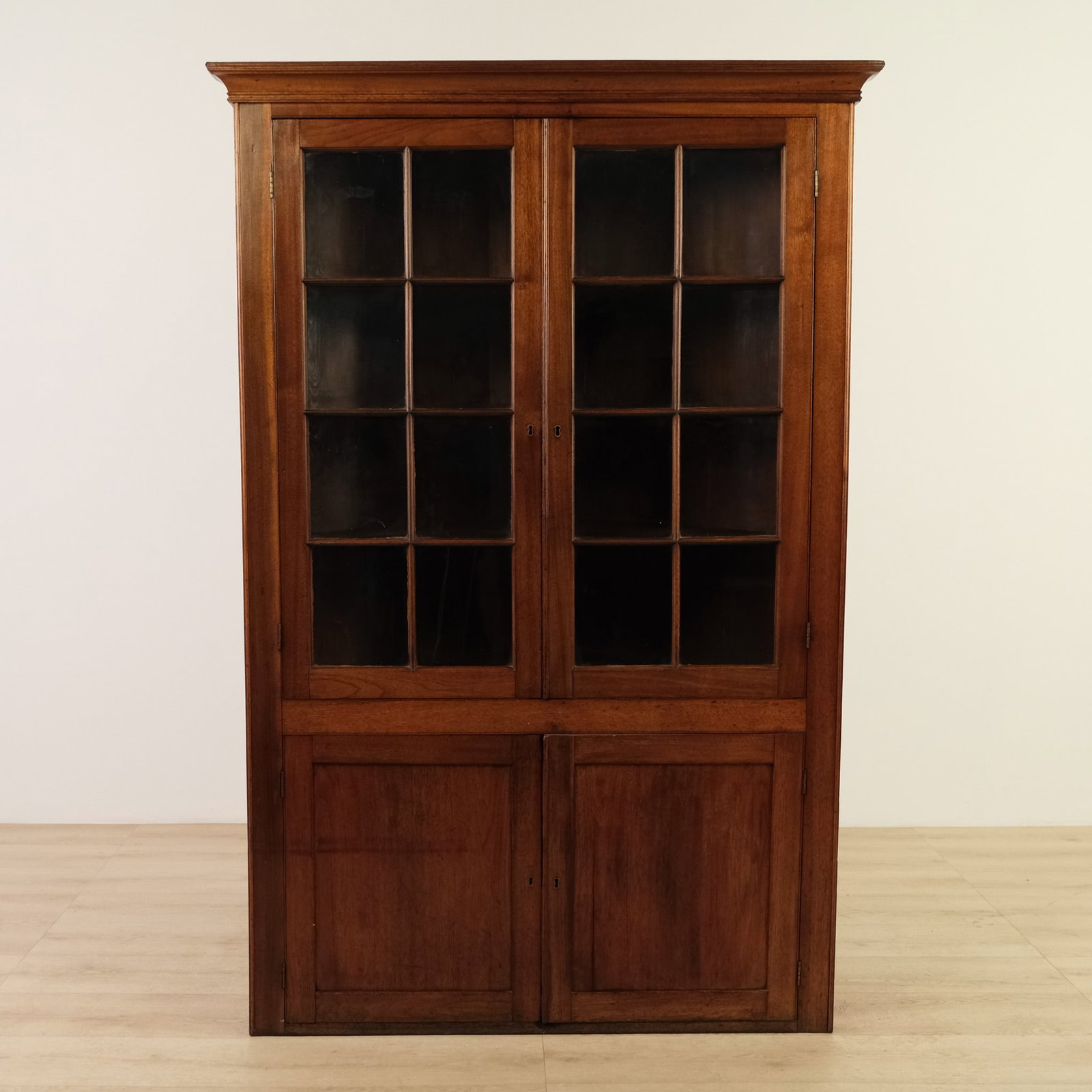 Mahogany Corner Cabinet: Upper portion features two glazed doors, each with multiple rectangular glass panes framed by wooden muntins. Lower section consists of two solid paneled doors for enclosed storage, and the entire cab