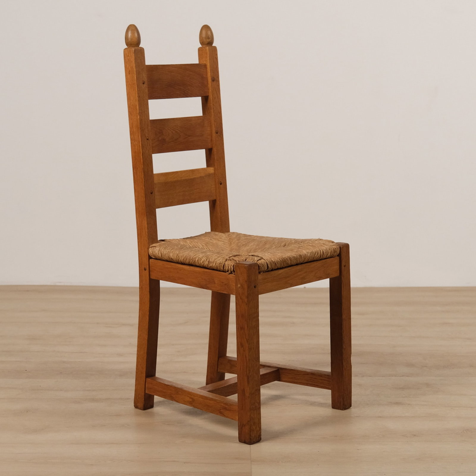 Set of Six French Oak Ladder Back Dining Chairs, c. 1940: Set of six substantial French oak ladder back dining chairs, each featuring a tall back with horizontal slats set between finial-topped stiles, and a woven rush seat. Square legs joined by box