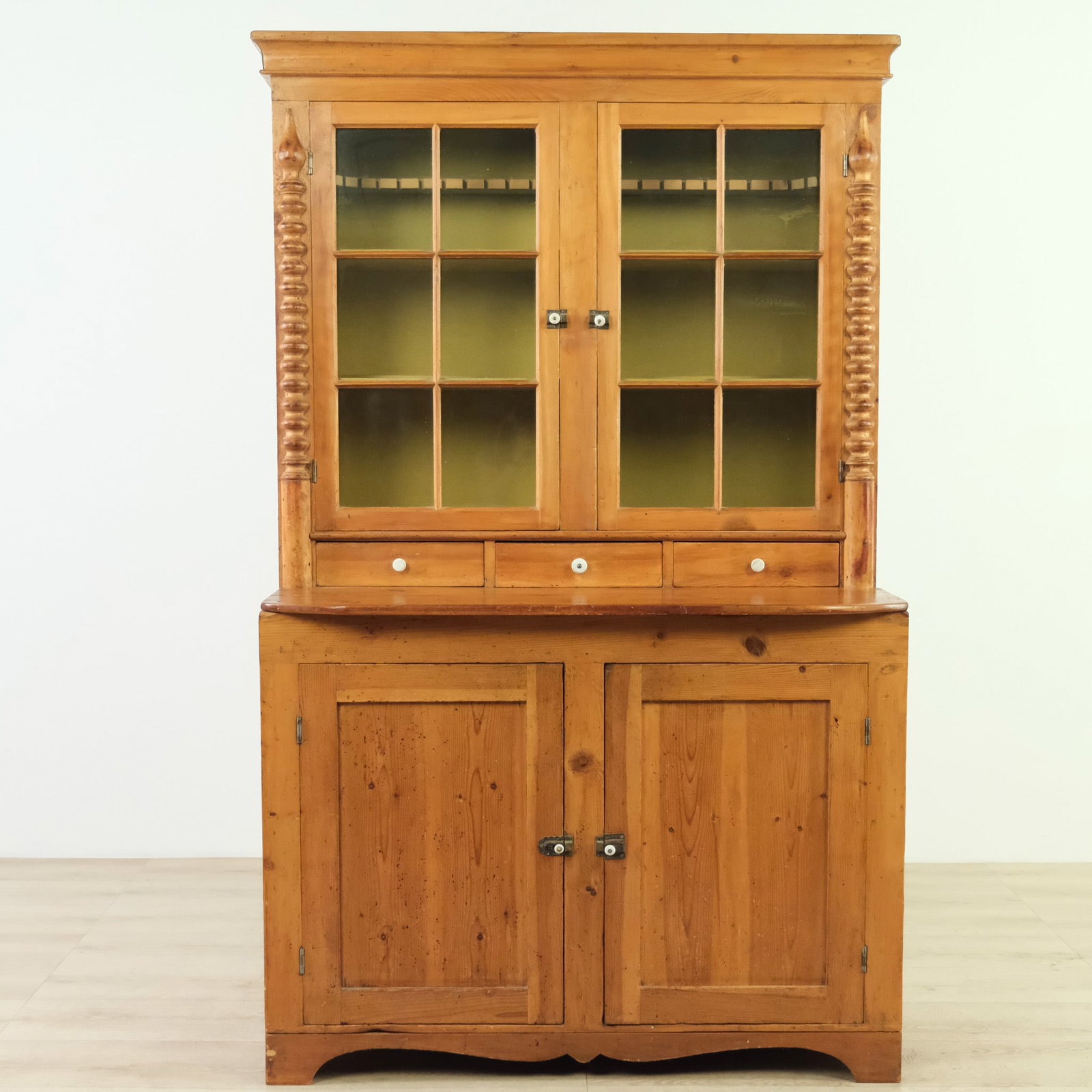 Primitive American Pine Country Cupboard, c. 1900: This 19th-century primitive pine cupboard features a warm honey-toned finish and classic American country style. The upper section has glass-paned doors flanked by decorative spool-turned columns,