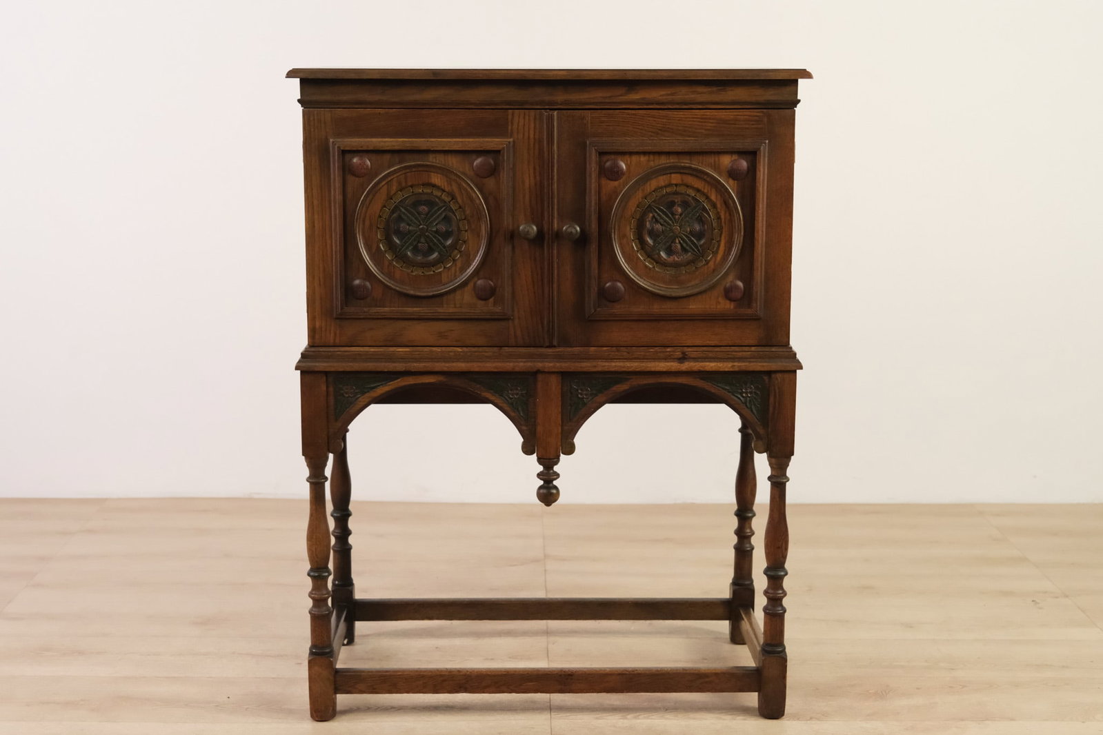 American Oak Jacobean Revival Style Cupboard: American Oak cupboard in a Jacobean Revival style, featuring two paneled doors with carved circular medallions, opening to a shelved storage compartment.