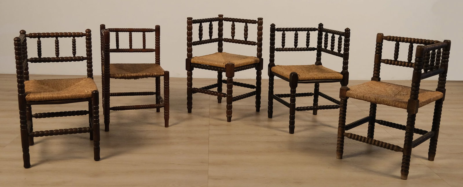 Dutch Oak & Rush, Bobbin-Turned, Corner Chairs, c. 1930s: This set of five corner chairs are crafted from dark, turned wood with elaborately spooled or bobbin-carved legs, stretchers, and uprights. Each chair features a distinctive square seat with rush or