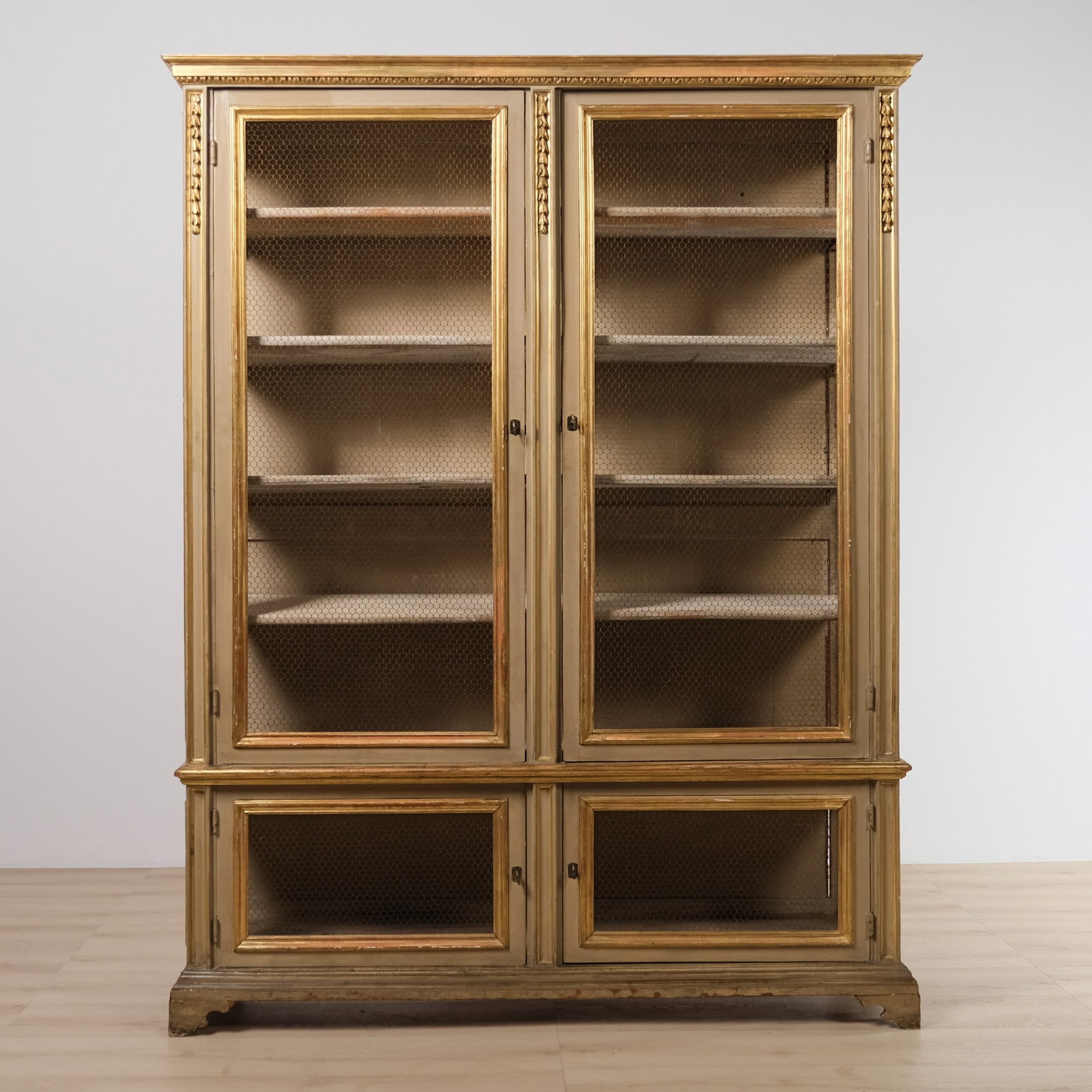 Large Italian Painted and Gilt Plate Cupboard: This impressive painted plate cupboard features wire-fronted doors set within a formal architectural profile, with a molded cornice, molded base, and gilded trim including carved rosette accents.